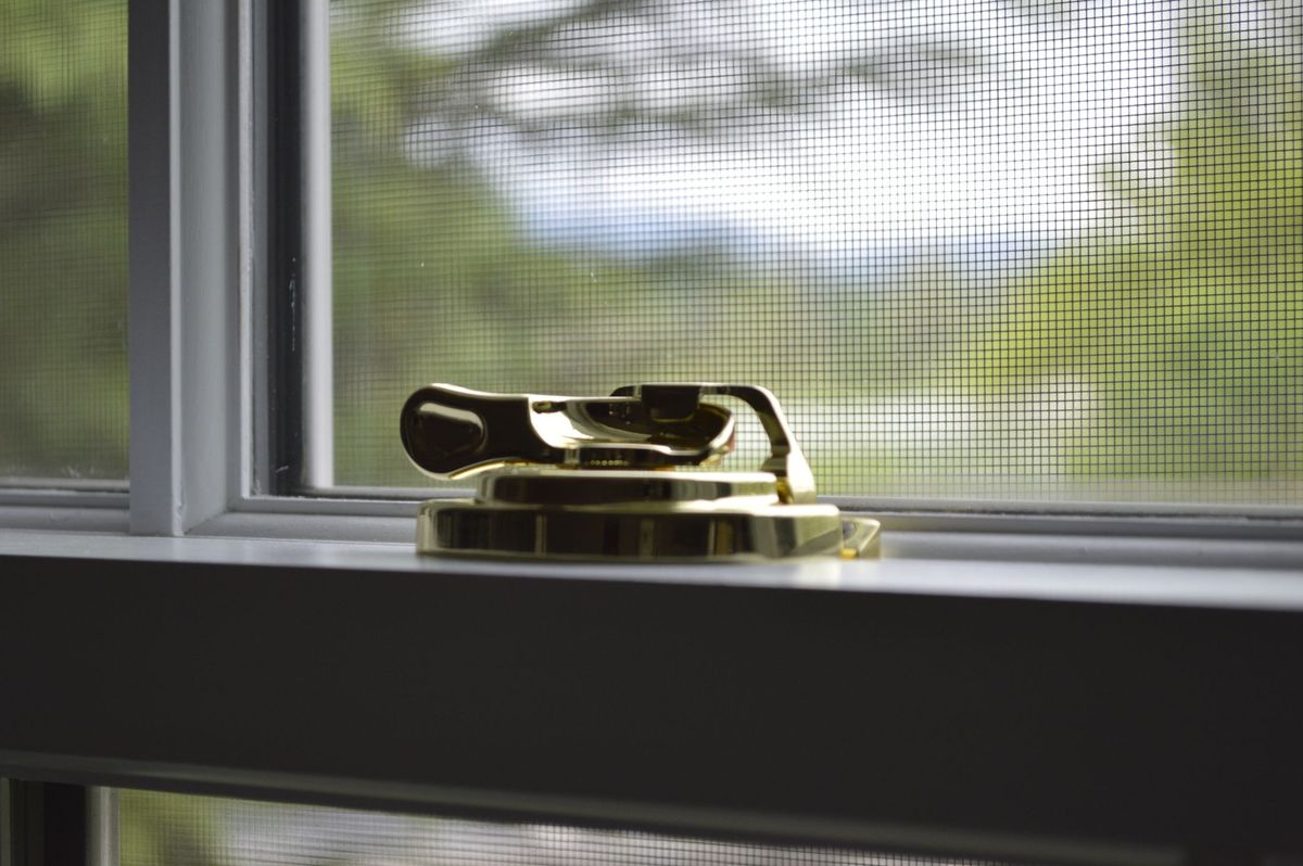 A window with a fly screen fitted behind the sash and a brass latch in front