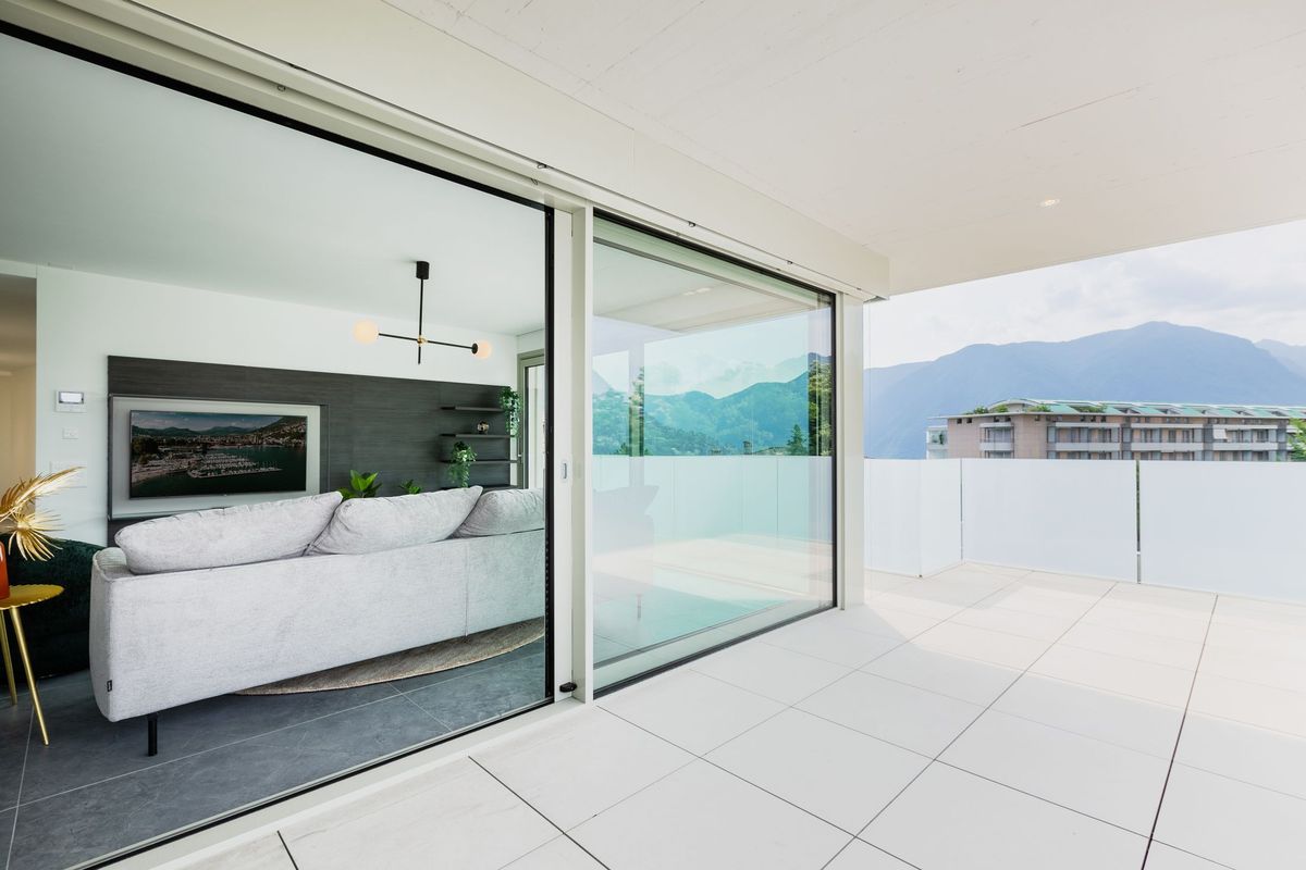 A wide sliding glass door opening onto a white terrace with mountains beyond