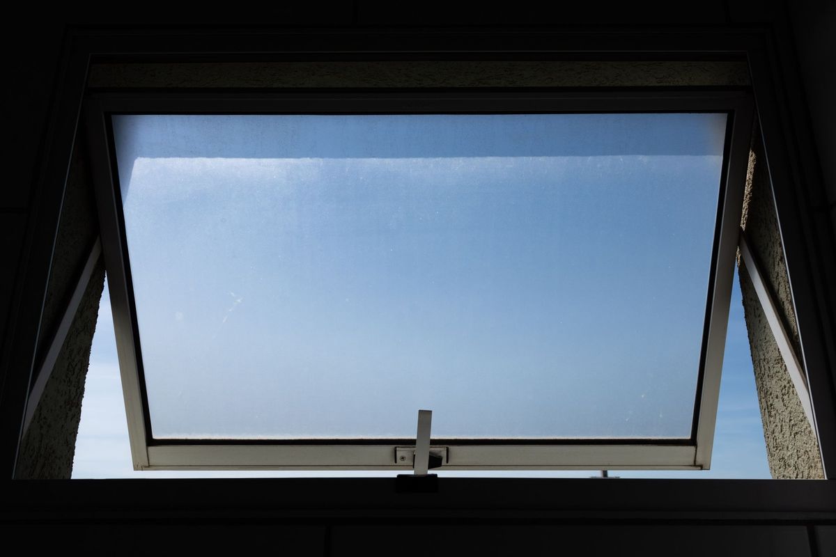 A top-hung window opened outwards against a clear sky, dark slim frame