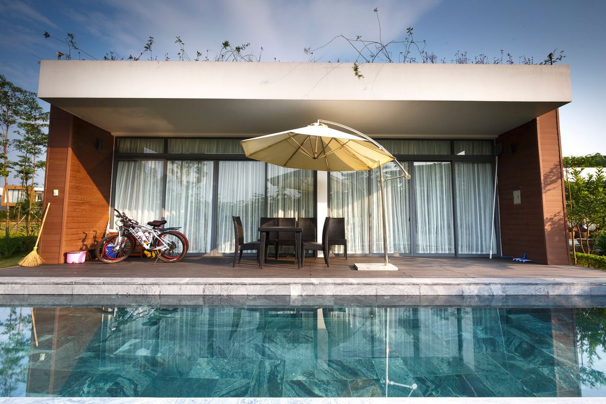 Flat-roofed house with full-width dark-framed sliding doors opening onto a swimming pool